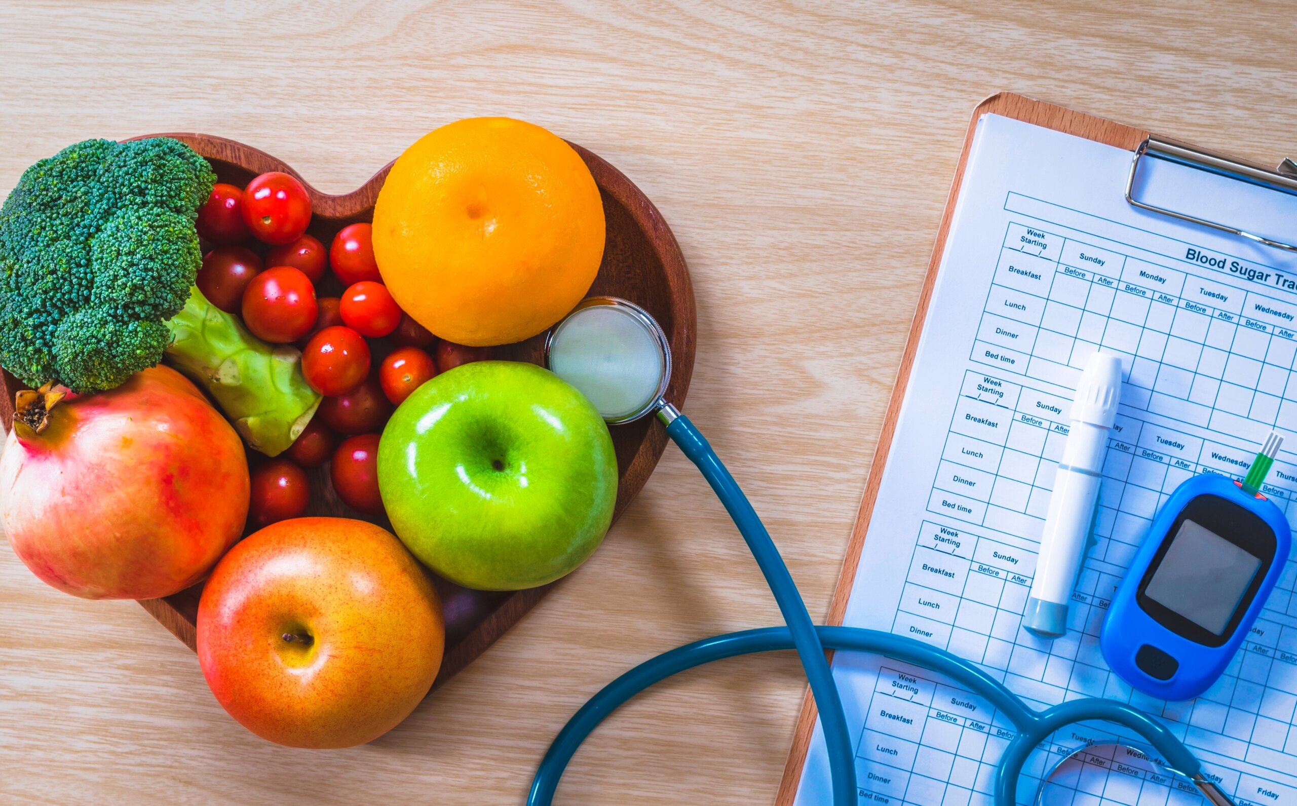 fruits and vegetables in a bowl beside a doctors pad, stethoscope, and diabetes machine